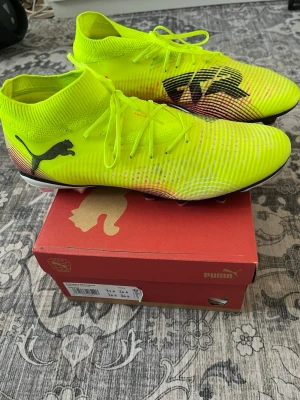  Puma Future 8 Pro - Säljer ett par neongula Puma fotbollsskor med svart logga och grafiskt mönster på sidan. Skorna har snörning och en strumpliknande krage för extra stöd runt ankeln. Ovandelen är tillverkad i ett syntetmaterial som ger bra bollkontroll och passform. Endast använda 2 gånger i träning, har knappast nån defekt 
