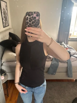 Svart ärmlös polotopp - Säljer en svart polotopp som är ärmlös och har en slim passform. Toppen har hög hals och är tillverkad i ett stretchigt material som sitter snyggt på kroppen❤️