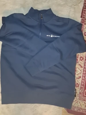 Mörkblå Sail Racing tröja med dragkedja - Mörkblå långärmad tröja från Sail Racing med halv dragkedja och hög krage. Tröjan har en stilren logga på bröstet och är tillverkad i ett mjukt material som passar perfekt till en avslappnad stil. Helt ny köpt förra veckan säljes för 500