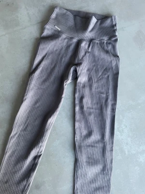 Grå ribbade leggings Aim'n - Grå ribbade leggings från Aim'n med i 7/8-dels längd. Perfekta för både träning och chill. Metallogon har lossnat på ena sidan men kan enkelt fästas med nål och tråd.