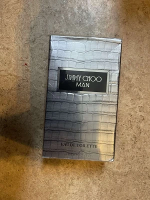 Jimmy Choo Man Eau de Toilette - Säljer en Jimmy Choo Man Eau de Toilette i en snygg silverfärgad förpackning med krokodilskinnsmönster. Doften är maskulin och modern, perfekt för dig som vill sticka ut. Förpackningen har en exklusiv känsla och är riktigt stilren.