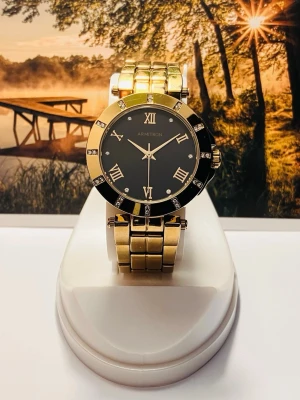 Guldig Armitron klocka med svart urtavla - Armitron klocka med guldig länk i metall och svart urtavla. Boetten är rund och dekorerad med glittrande stenar samt romerska siffror. En riktigt snygg accessoar med lyxig känsla och klassisk design.Nyligen servad med nytt batteri, säljes i befintligt skick enligt bilderna!