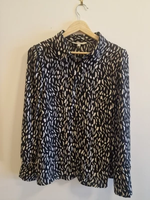 Svartvit mönstrad skjorta Cellbes - Svart skjorta från Cellbes med vitt abstrakt mönster. Klassisk krage, långa ärmar och knäppning framtill. Skjortan har en lös och bekväm passform, perfekt för en trendig och avslappnad stil.