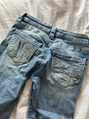 Ljusblå bootcut jeans med fickdetaljer - Säljer ett par ljusblå lågmidjade bootcut jeans med breda ben och coola V-formade sömmar på bakfickorna. Strl 158 men passar mig som vanligtvis har strl xs/s och är ca 1,67 lång. Skriv gärna prisförslag 💕