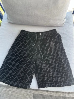 Svarta Fendi shorts och T-shirt  med logomönster - Snygga svarta shorts och T-shirt från Fendi med heltryckt FF-logomönster. Shortsen har en elastisk midja och är tillverkade i ett lätt och bekvämt material, perfekt för sommaren. 