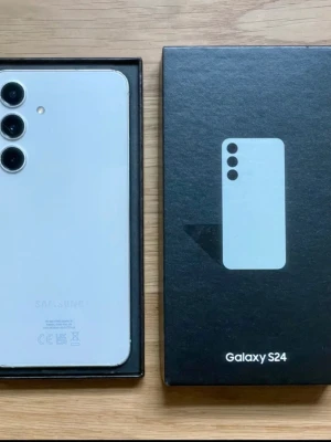 Samsung Galaxy S24 vit Android-mobil - Samsung Galaxy S24 i snygg vit färg med stilren design och rundade hörn. Baksidan har tre kameror i rad och glasfinish. Mobilen har en stor skärm och tunna kanter, perfekt för dig som gillar modern teknik och Android.