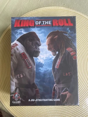 King of the Roll brädspel - King of the Roll är ett brädspel med jiu-jitsu-tema från Gaard Games. Spelet har en cool omslagsdesign med en gorilla och en person i kampsportsdräkt, och titeln i rött och vitt. Perfekt för dig som gillar strategi och kampsport.
