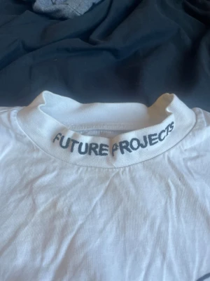 Vit Future Projects t-shirt med tryck - Vit t-shirt från Future Projects med svart tryck på kragen och ett diskret logotryck på bröstet. Klassisk passform och rund halsringning. Perfekt för en clean och stilren look. Kontakta gärna ❤️ 