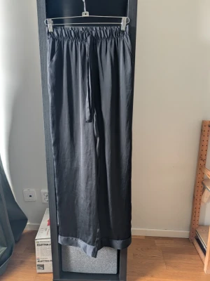 Svarta vida linnebyxor med dragsko - Snygga svarta linnebyxor med avslappnad passform och dragsko i midjan. Byxorna har raka ben och resår i midjan för extra komfort. Perfekta för en chill och stilren look. Enligt förra säljaren från Kookai