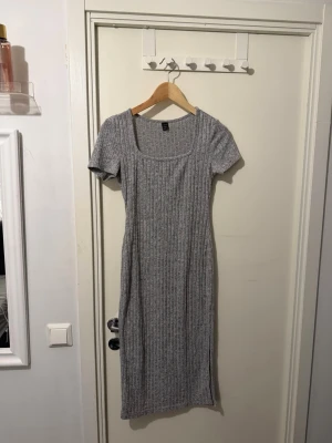Grå ribbad klänning från SHEIN - Grå ribbad klänning från SHEIN med korta ärmar och fyrkantig ringning. Klänningen är figurnära och har en enkel, stilren design som passar perfekt till många olika looks. Tillverkad i mjukt material för skön känsla.