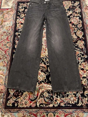 Grå wide leg jeans från Gina - Säljer ett par gråa wide leg jeans med klassisk femficksdesign och raka ben. Jeansen har en lätt tvättad look och är tillverkade i denim. Perfekta för dig som gillar en avslappnad och trendig stil.