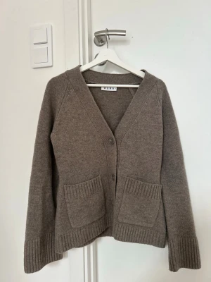 Brun kofta från WERA med fickor - Brun kofta från WERA med v-ringning och knäppning framtill. Koftan har två stora ribbstickade fickor och ribbade muddar vid ärmslut och nederkant. Använd enstaka gånger, nypris 899kr