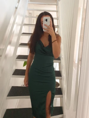 Mörkgrön satinklänning - Elegant mörkgrön klänning i satin med smala axelband, draperad halsringning och en snygg slits framtill. Klänningen har en figurnära passform!!