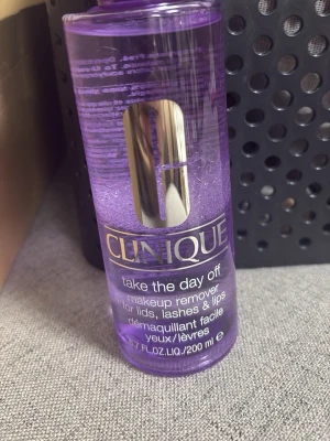 Clinique Take The Day Off remover - Lila makeup remover från Clinique i plastflaska, perfekt för att ta bort smink från ögon, fransar och läppar. Innehåller 200 ml och har en stilren design med silvrig logga på framsidan.
