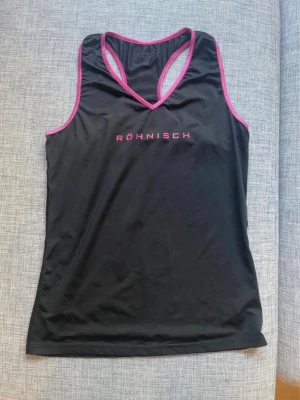 Träningslinne M från Röhnisch - Ett svart träningslinne med rosa kanter från Röhnisch.  Storlek M Material: polyester och elestan