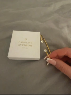 Guldarmband Caroline Svedbom - Snyggt och stilrent armband från Caroline Svedbom i gul med två gnistrande kristaller i ändarna. Öppen design som gör det lätt att ta på och av. Perfekt accessoar för att lyfta din outfit med lite extra bling. Använt 1 gång! Fri frakt !!