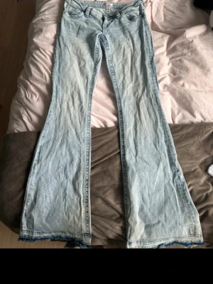Ljusblå bootcut jeans - Säljer ett par ljusblå bootcut jeans i klassisk denim med fickor och knappgylf. Jeansen har en utsvängd passform nedtill. Dem är uppsprättade vid benen. 