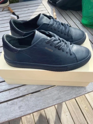 Svarta sneakers från Axel Arigato - Stilrena svarta sneakers från Axel Arigato i läder med diskret guldfärgad logga på sidan. Klassisk låg modell med svarta skosnören och svart sula. Perfekta för en clean och modern look. De är nästan helt nya och skriv ifall du är intresserad😃