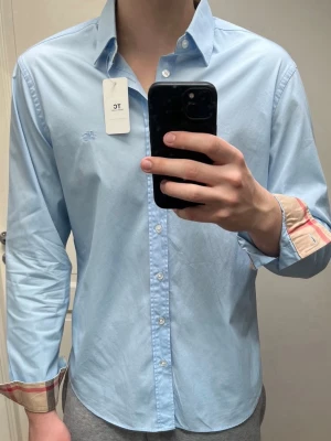 Ljusblå burberry skjorta storlek L - Super fin ljusblå burberry skjorta i storlek L, som är i ny skick utan tecken på användning. Nypris 5000kr mitt pris endast 1100kr. Hör gärna av er vid frågor eller funderingar. Mvh Trend closet😊