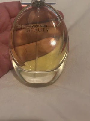 Calvin Klein Beauty parfym - En elegant parfym från Calvin Klein med namnet Beauty. Flaskan är oval och genomskinlig med silvrig kork och innehåller en ljusgul vätska. Perfekt för dig som gillar stilrena och klassiska dofter.