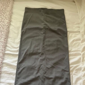 Grå långkjol med slits - Snygg grå långkjol i enkel och stilren design. Kjolen har en rak passform och en diskret slits baktill som ger extra rörelsefrihet. Perfekt att matcha med både sneakers och boots. Aldrig använd. 