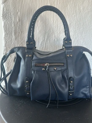Oanvänd handväska  - Snygg handväska i skinn. Aldrig använd. Många fack. Axelrem finns med. Mörkblå. 