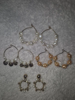 Flera örhängen med pärlor och detaljer - Säljer ett set med 4 par örhängen i olika stilar. Alla har pärlor i vitt eller guldton, vissa med små myntdetaljer och andra med guldfärgade inslag. Perfekta för att mixa och matcha till olika looks. Materialet är metall och pärlor.