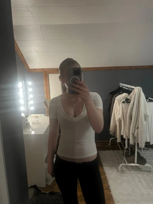 Vit v-ringad topp från Gina Tricot - Vit, tight och basic topp från Gina Tricot med djup v-ringning och korta ärmar. Tillverkad i mjuk bomullsmix som sitter skönt mot kroppen. 