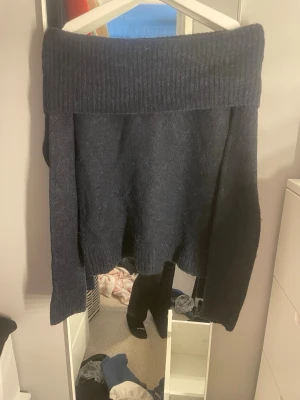 Mörkblå off shoulder stickad tröja - Mysig mörkblå stickad tröja från Gina Tricot med bred ribbad off shoulder-krage. Tröjan har lång ärm och är gjord i ett mjukt, luddigt material som känns skönt mot huden. Perfekt för kalla dagar när du vill vara både varm och snygg.