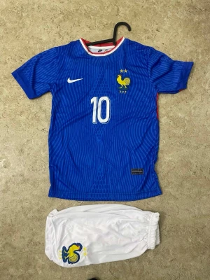 Frankrike Mbappé matchställ Nike - Säljer ett blått Frankrike fotbollsställ från Nike med Mbappé och nummer 10 på ryggen. Tröjan har vita och röda detaljer, FFF-logga och två stjärnor. Tillhörande vita shorts med FFF-logga. Perfekt för dig som älskar fotboll och landslaget.