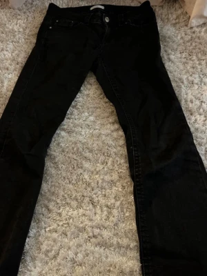 Svarta bootcut jeans - Säljer ett par svarta jeans med bootcut passform och klassisk femficksdesign. Jeansen har knappgylf och bälteshällor, perfekta till en avslappnad stil. Materialet känns som bomull med lite stretch för extra komfort. Små i storleken