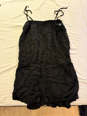 Svart kort jumpsuit med knytband - Svart jumpsuit. Banden är knutna, går och justera banden.
