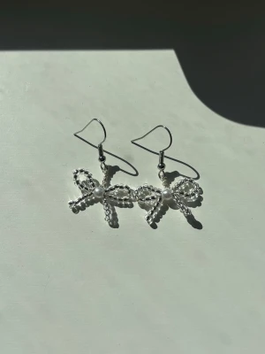 Silvriga rosettörhängen med pärlor - Snygga örhängen i form av rosetter, gjorda av små silvriga/genomskinliga pärlor och med en vit pärla i mitten. Hängande modell med krokfäste.