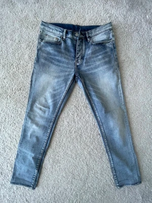 Blå slim fit jeans från MNML - Säljer ett par blå slim fit jeans från mnmlmed snyggt slitna detaljer och klassisk femficksdesign. Jeansen har en ljus tvätt och raka ben. Dem är helt nya från MNML och är väldigt snygg.