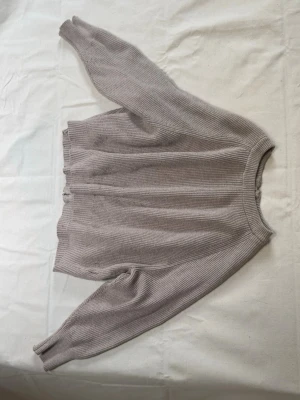 Beige ribbad ziptröja med dragkedja på ryggen  - Mysig beige ribbad tröja med dragkedja baktill. Tröjan har långa ärmar, rund halsringning och breda muddar vid ärmslut och nederkant. 