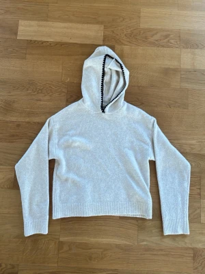 Beige hoodie från Kappahl - Mysig beige hoodie från Kappahl med svart dekorationssöm längs huvan. Tillverkad i mjukt material, perfekt för chill dagar. Långärmad modell med ribbade muddar vid ärmslut och nederkant. Enkel och stilren design som passar till det mesta.