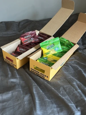 Koffein godis och elektrolyt godis (NoBox) - Två lådor energigodis från Nobox, en med Sour Cola och en med Pick Me Up (Pear). Godiset är förpackat i portionspåsar och innehåller koffein, BCAA och elektrolyter. Sour Cola har brunröd påse och Pick Me Up har grön påse. Perfekt för extra energi under dagen. 16 elektrolyt godis påsar och 14 elektrolyt. Säker eftersom jag vill sänka mitt koffein intag och elektrolyter har jag i nuläget inte behov av. Orginal pris 25kr per påse. Hör av vid frågor!