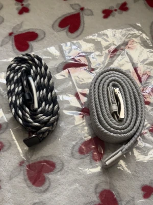 Två flätade bälten i svart och grått - Säljer två snygga flätade bälten, ett i svart och vitt mönster och ett i ljusgrått. Båda har silvriga spännen och detaljer i konstläder. Perfekta för att ge outfiten en cool touch.