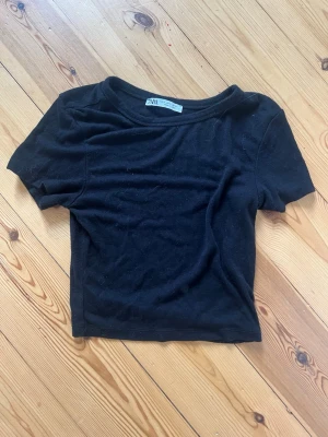 Svart cropped t-shirt från ZARA - En svart, enkel cropped t-shirt från ZARA med rund halsringning och korta ärmar. T-shirten är i mjukt bomullsmaterial och har en klassisk, stilren look som passar till det mesta. Perfekt till jeans eller kjol för en avslappnad vibe.