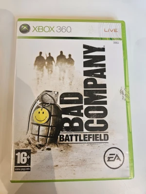 Battlefield: Bad Company Xbox 360 - Battlefield: Bad Company till Xbox 360 är ett actionfyllt FPS-spel med taktisk förstörelse och online multiplayer. Omslaget är vitt med en grön plastbox och visar en handgranat med smiley och soldater i bakgrunden. Spelet är PEGI 16+ och utvecklat av DICE.