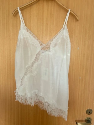 Vit spetslinnetopp med v-ringning - Säljer en vit linnetopp med tunna axelband och v-ringad hals. Toppen har dekorativa spetsdetaljer längs ringningen och nederkanten som ger en romantisk vibe. Perfekt att bära som den är eller under en kavaj. Aldrig använd! Pris går att diskutera 