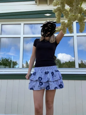 Blåvit volangkjol med blommor - Söt kort volangkjol med blå och vita ränder samt blommigt mönster. Kjolen har resår i midjan och är perfekt för varma dagar. Lätt och luftig känsla, passar till många olika toppar.🩵Fån Lindex Egan märke Holly & Whyte i storlek M.