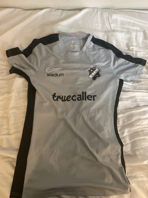 Grå AIK fotbollströja från Nike - Säljer en grå AIK matchtröja från Nike med svarta detaljer längs sidorna och axlarna. Tröjan har AIK:s klubbmärke på bröstet, samt tryck från Truecaller, Stadium, Fabege och SVEA. Tillverkad i ett lätt och ventilerande material, perfekt för träning eller match. Slim Fit Storlek S