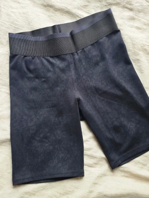 Svarta cykelshorts med bred resår - Snygga svarta cykelshorts med bred ribbad midjeresår. Shortsen är tillverkade i ett stretchigt syntetmaterial som sitter tight och bekvämt. Perfekta för träning eller en sportig look. Inga synliga loggor eller mönster.