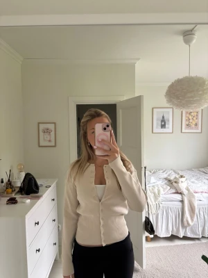 Beige ribbad kofta med knappar - Snygg beige kofta som är ribbad och knappar hela vägen framtill. Modellen är figurnära och har långa ärmar. Perfekt att styla över ett linne eller t-shirt för en clean och enkel look.