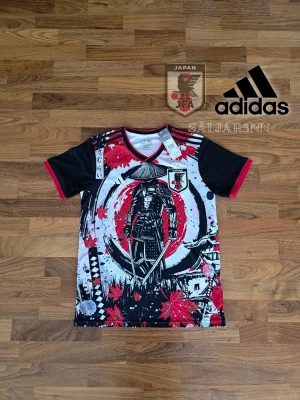 Japan Fotbollströja - Japan Samuraj Fotbollströja – Limited Edition från Adidas. Unik tröja i storlek S, inspirerad av japansk kultur och officiellt licensierad av JFA. Design med samuraj, lönnlöv och starka färger i rött, svart och vitt. Helt ny och perfekt för fans, cosplay eller streetwear. 100 % polyester – lätt och snabbtorkande.  📦 Snabb leverans – skickas samma dag! Kontakta mig vid intresse! 📌 
