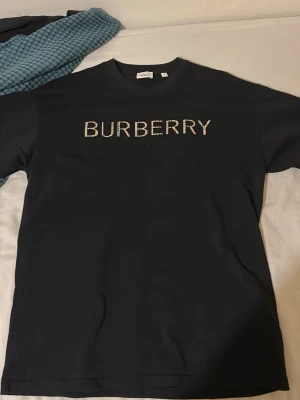 Svart Burberry t-shirt med logga - Snygg svart t-shirt från Burberry med stor logga i vitt på bröstet. Klassisk rund halsringning och korta ärmar. Tillverkad i mjuk bomull för skön känsla och stilren look.