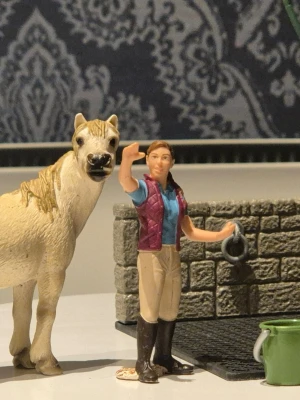 Schleich paket - Säljer en naturtrogen leksakshäst i beige plast med ljusbrun man och svans samt en stallfigur med vinröd väst, blå tröja och ridbyxor. Samt en spolspilta med tillbehör 