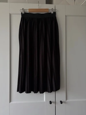 Svart plisserad långkjol från JDY - Snygg svart plisserad långkjol från JDY. Kjolen har resår i midjan och ett elegant fall med tydliga veck. Perfekt för dig som gillar en stilren och enkel look. Passar till många olika outfits och är lätt att matcha.