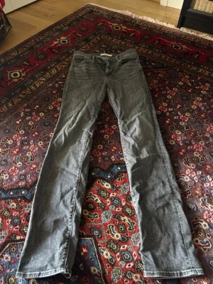 Grå Levi's jeans raka ben - Säljer ett par grå jeans från Levi's med klassisk femficksmodell och raka ben. Jeansen har en diskret tvättad look och Levi's ikoniska bakficka med V-söm. Perfekta för dig som gillar en enkel och tidlös stil.